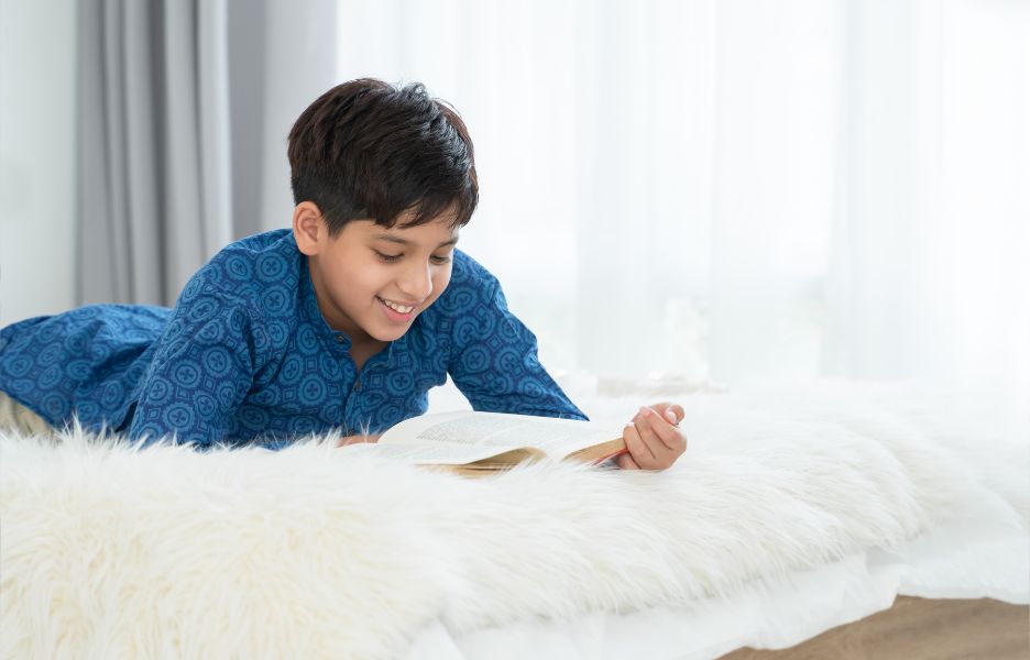10 year old boy lying on a white bed, enjoying reading a book
