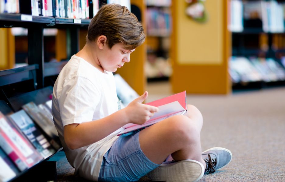 Boy sitting on the floor reading in a library