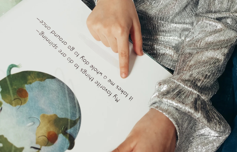 A child reading a picture book, using their finger to following the words.